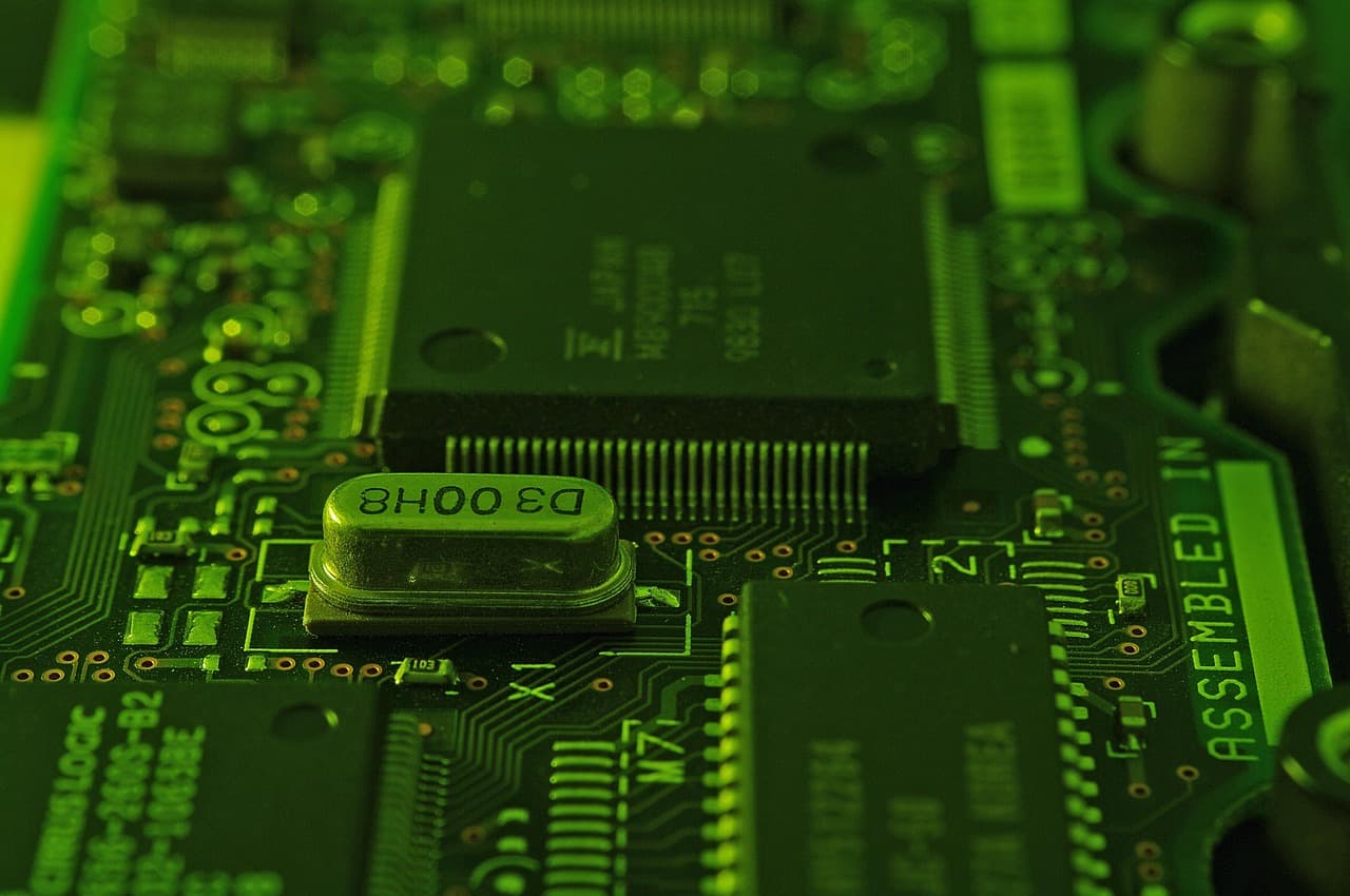 An extreme close-up of a green circuit board with dense silver microchip circuitry, representing the analog and mixed-signal semiconductor components at the center of Analog Devices' business