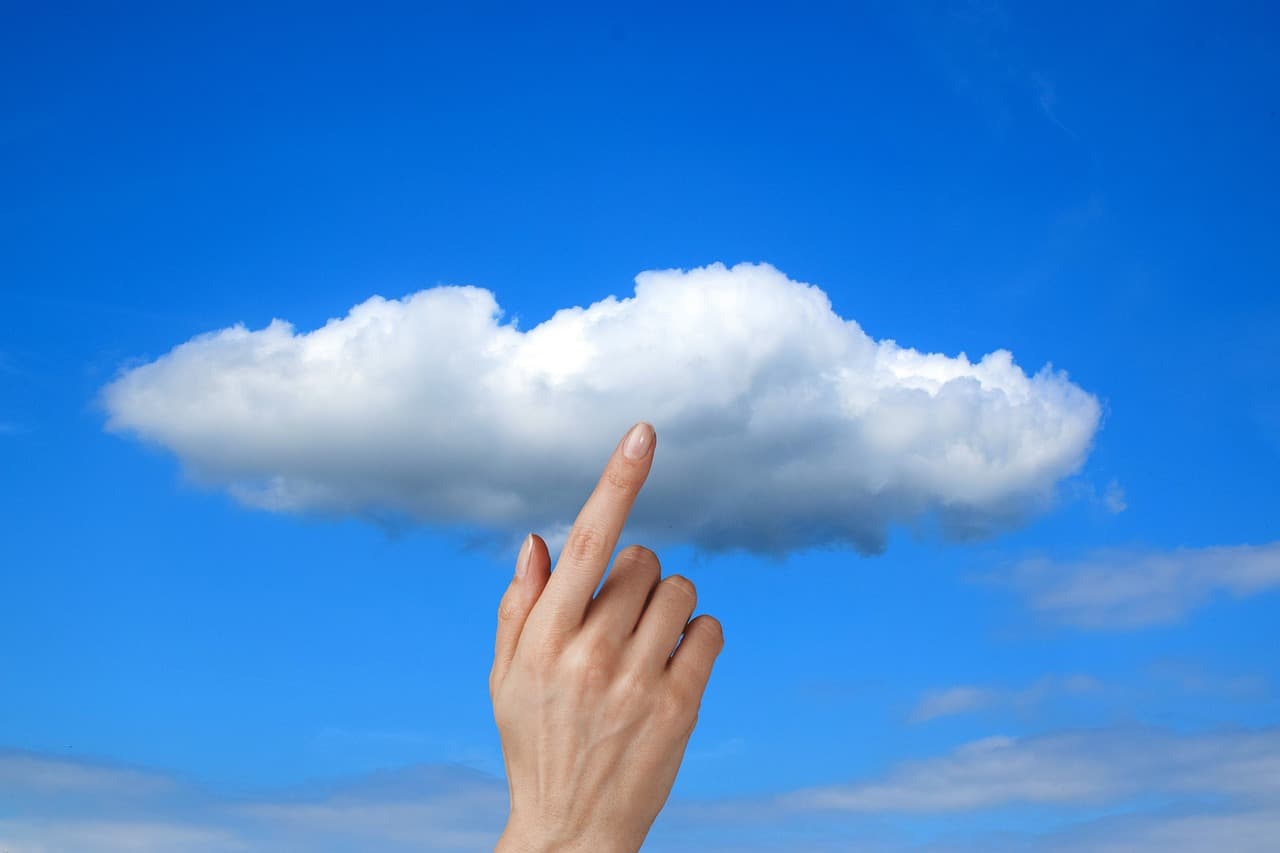 A hand reaching toward a glowing cloud symbol against a blue background, representing the cloud infrastructure Oracle is racing to build to service its AI backlog.