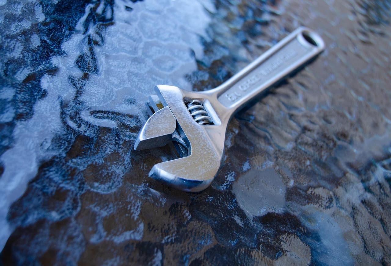 A chrome adjustable wrench resting on a wet workbench surface, representing the tools and hardware at the center of Home Depot's business